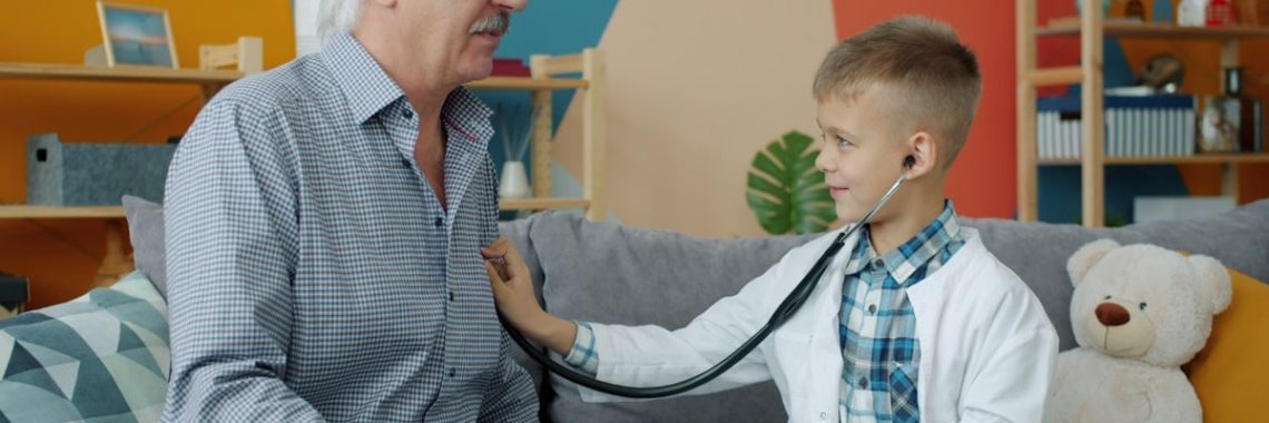 Adorable child is playing with grandfather examining with stethoscope in apartment having fun together indoors. Medicine, childhood and leisure activities concept.